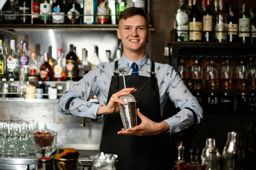 young smiling barman preparing glass and shaker to make cocktail.