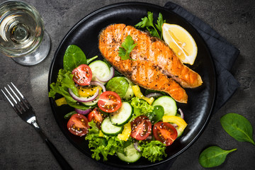 Grilled salmon fish steak with vegetables on black.