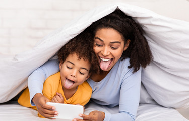 Joyful Mother And Daughter Playing Mobile Games Lying In Bed