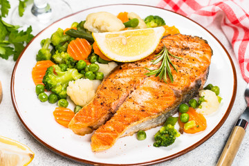 Grilled salmon steak with vegetables on white.