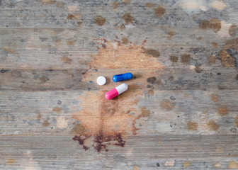 A blue capsule and a capsule of white and red color with a white tablet are in the center of a table with spots reminiscent of the spread of the disease.