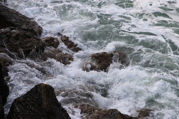 Coastal water breaking over surface of jagged rocks