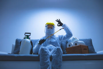 Scientist with protective suit and face mask, bio hazard sprayer for decontamination agaist viruses, germs - toilet paper stock paranoia at home, waiting for end of days. - obrazy, fototapety, plakaty