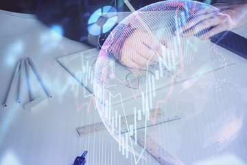 Double exposure of man's hands writing notes of stock market with forex chart.