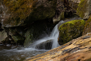 A beautiful small waterfall in a thicket of forest on high hills among huge boulders covered with moss