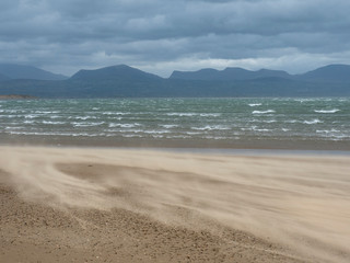 Beach with strong wind that blows up the sand with sea and mountains in the background