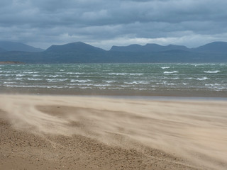 Fototapeta na wymiar Beach with strong wind that blows up the sand with sea and mountains in the background