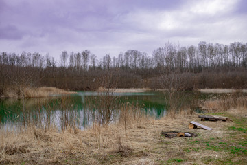 Obraz na płótnie Canvas A flooded old sand pit in early spring with blue water in cloudy weather - nature captures anthropogenic culture over time.