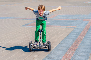Fashionable happy child teen boy rides a segway in square with his arms outstretched to side....