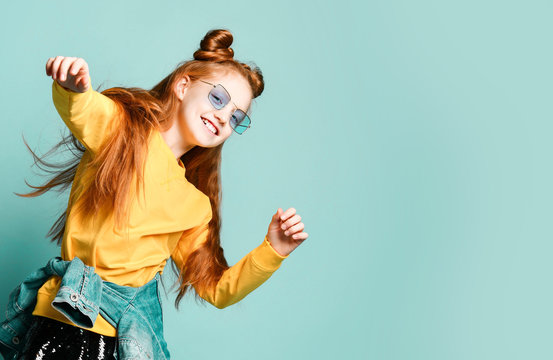 Happy red-haired teen girl in yellow sweatshirt and glossy black skirt feels good dancing active