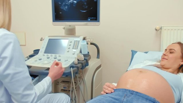 A doctor transmits a photograph of ultrasound scanning a happy couple, they watch photo and smiling