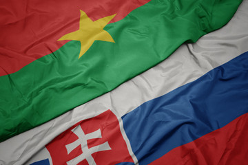 waving colorful flag of slovakia and national flag of burkina faso.