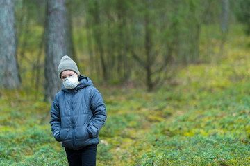 Disappointed lonely kid wearing mask for protection of corona virus spread on a empty forest.