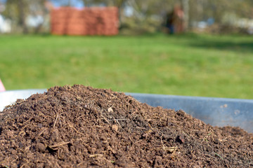 Fresh compost in a wheelbarrow with a green meadow in the background