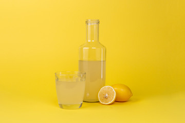 Bottle with lemon juice and a glass next to it and whole and sliced lemons isolated on a yellow background