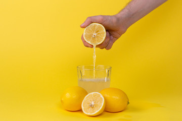 squeezing lemon juice into glass on yellow background