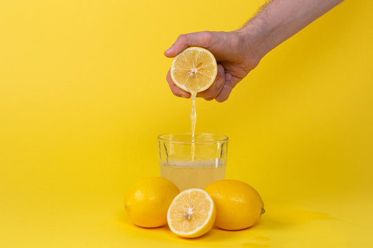 Squeezing Lemon Juice Into Glass On Yellow Background