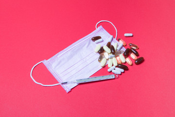 pink medical face mask, mercury thermometer and tablets on red background