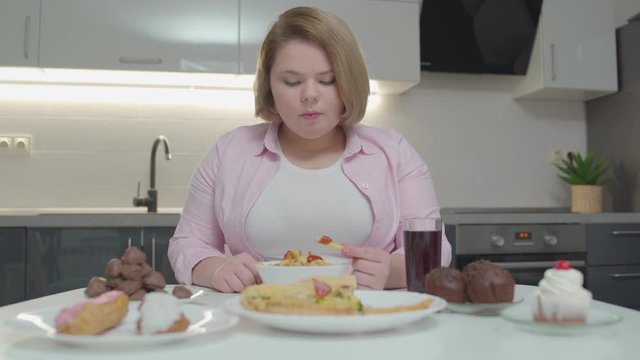 Obese woman eating french fries and drinking soda, pizza and cakes on the table