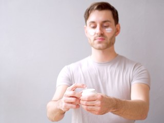 Young man taking care of his skin with a hydration cream and lotion closeup, background.