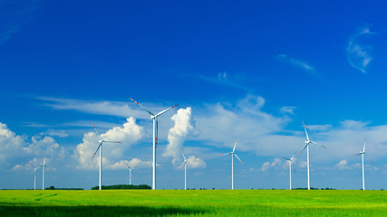 Windmills on a green field, on a bright sunny and windy day with forming cumulonimbus