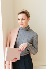 Indoor portrait of beautiful woman wearing pink coat on one shoulder, smiling, reading pink book place your text for advertising. copy space mockup 