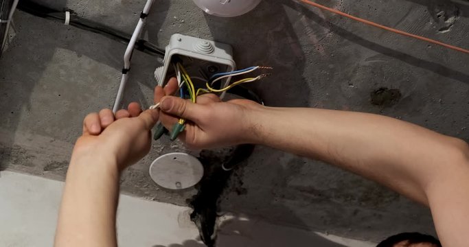 Male electrician manually twists electrical wires in junction box, puts on an insulating rubber black cap, does not use tools, replacing wiring, major repairs of room, energy, electrical work