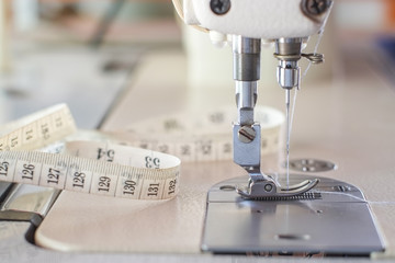Needle presser foot with blue thread of white industrial sewing machine use sew cloth and tape measure close-up.