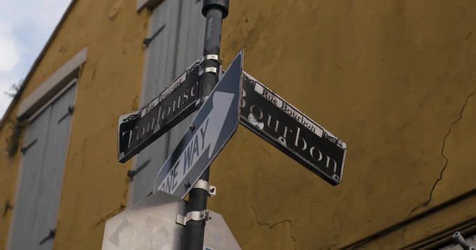 New Orleans Street sign at the corner of Bourbon and Toulouse with NOLA Decor in the background as they move in slow motion.