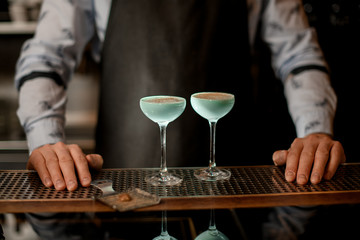 Two glasses with light blue drink stand on bar