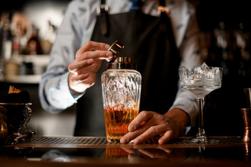 Close-up glass shaker with brown alcoholic drink and ice.