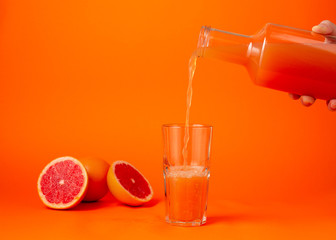 Pouring the grape juice in the glass over orange gradient background