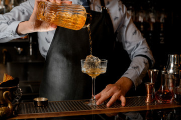 Close-up how barman in black apron pours drink from shaker into glass.