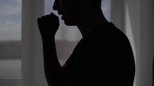 Silhouette of a coughing man on a window background. The patient is treated at home for the virus Covid-19