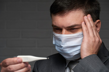 man measures body temperature with a thermometer, checks his health status, has a protective face mask - healthcare and medicine concept
