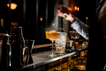 Bartender's hand carefully sprinkles on glass with brown alcoholic cocktail.