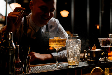 young smiling barman sprinkles on glass with ice alcoholic drink