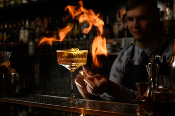 Fototapeta na wymiar Young bartender carefully spray and makes fire over glass with cocktail