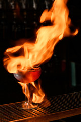Close-up of glass with cocktail on fire stands at bar counter.