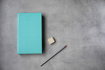 Libro azul,  lapis y goma sobre mesa gris