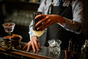 Barman holds shaker by hand over glass with cocktail.