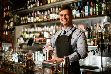 young smiling bartender in black apron preparing to make cocktail.