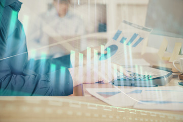 Double exposure of graph with man typing on computer in office on background. Concept of hard work. Closeup.