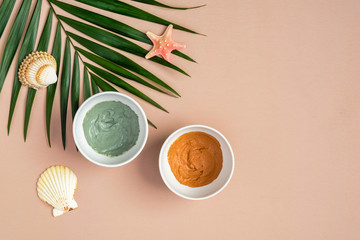 Obraz na płótnie Canvas Homemade clay masks in bowls and tropical palm leaf on peach background. Natural organic SPA cosmetic product, face skin care, beauty treatment concept. Flat lay, top view.