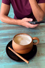 man hands with smartphone and cappuccino mug with coconut milk on table, Koh Kood island, Thailand