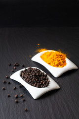 Healthy food and alternative medicine ingredient concept organic Black peppers and turmeric powder in square ceramic cup on black slate stone board with copy space.