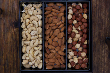 Box with three kinds of nuts, cashews, hazelnuts, almonds. Wooden background. Top view.