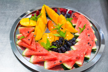Fruit plate with watermelon, melon, grapes and orange. Metal tray on a gray background.