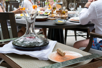 Decanter with red wine. In the background is an open-air restaurant.