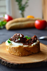 French baguette with cream cheese and dried tomatoes on a dark background.